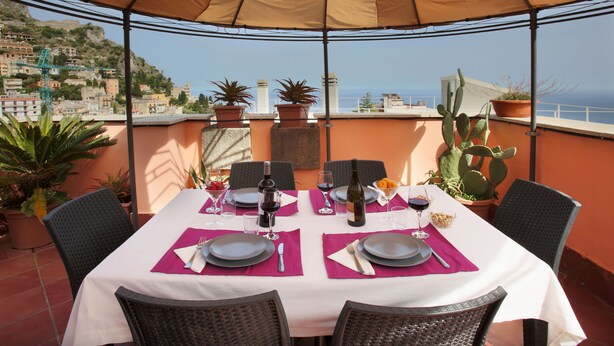 A dining table set for two with a view of the sea and buildings in the background. - Spacious 4 BR apartment, Taormina center, multiple terraces w. stunning views  (Taormina)