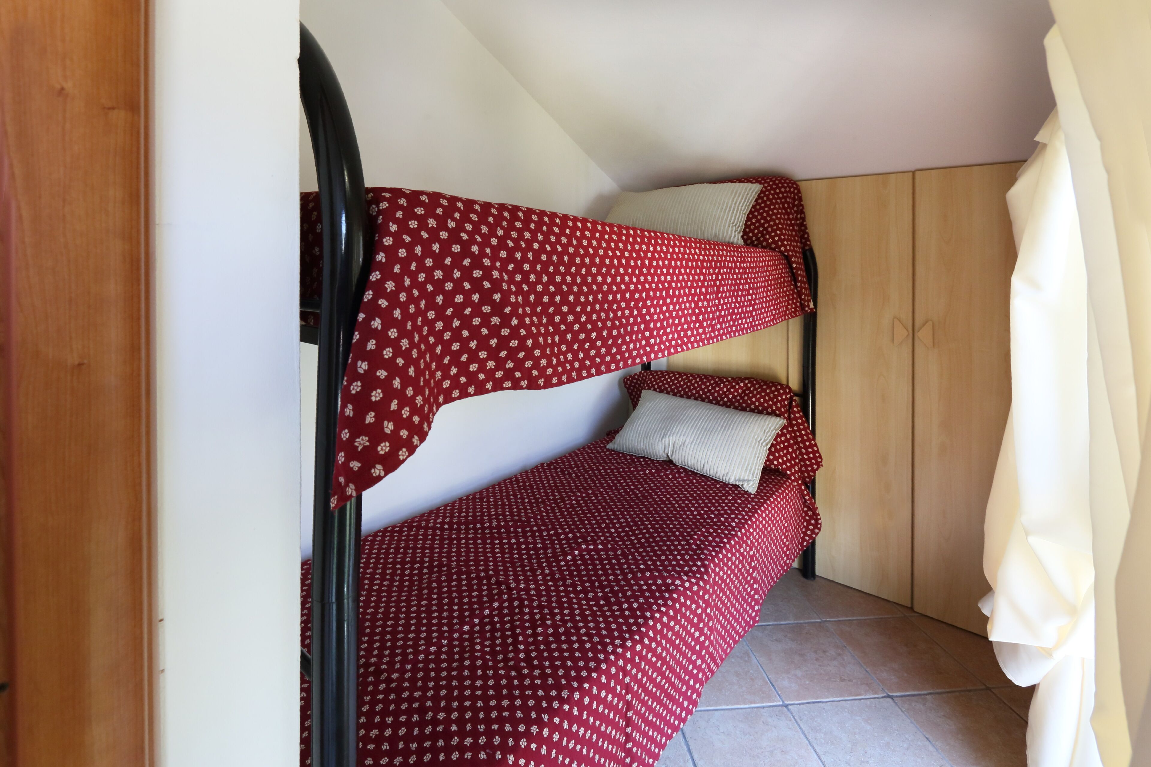 A bunk bed with red bedding and a wooden wardrobe in the background.