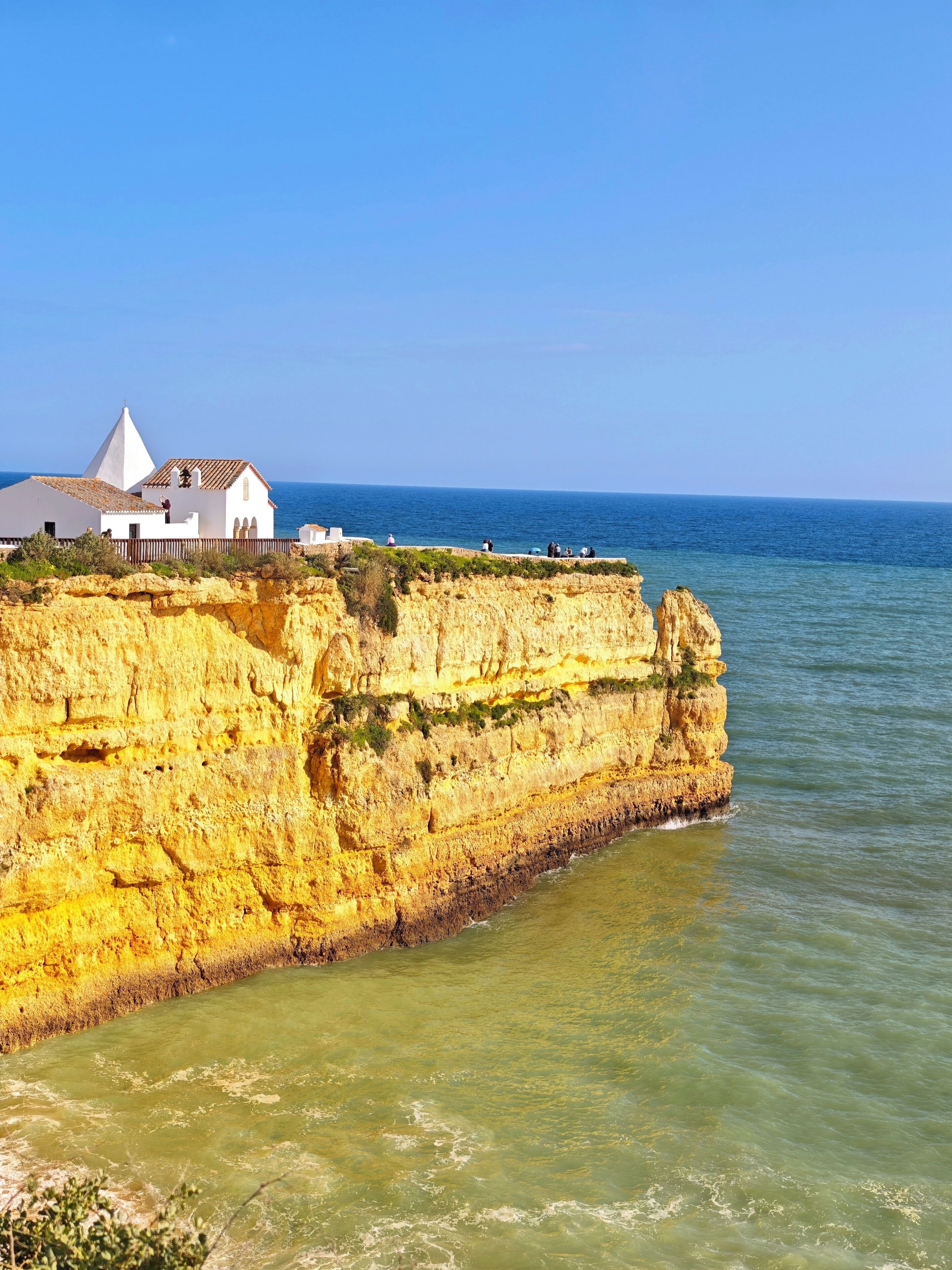 A coastal cliff with a white building featuring a conical roof, overlooking the sea.