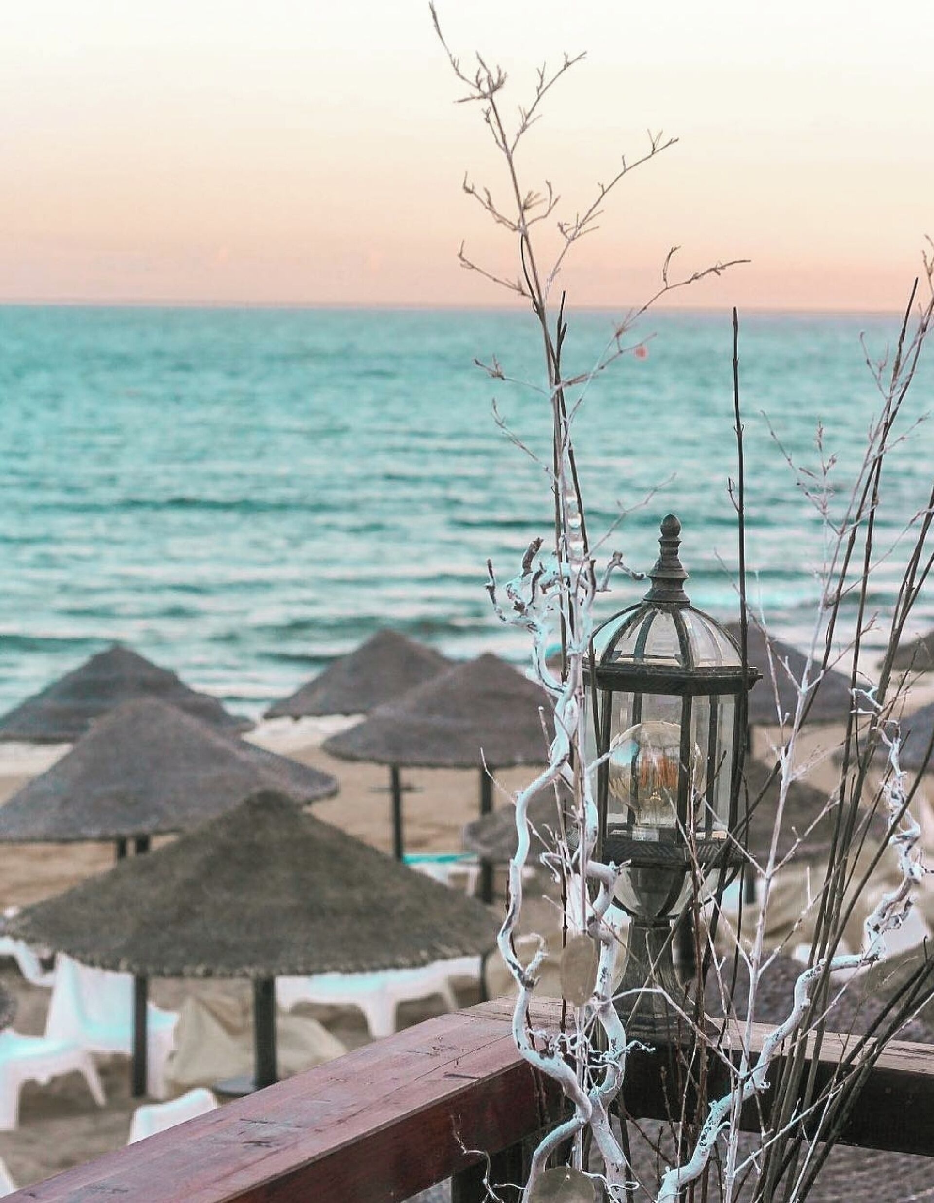 A beach scene with a wooden railing, a glass lantern, and thatched umbrellas.