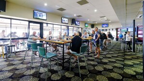 A restaurant with multiple tables and chairs, large windows, and several televisions mounted on the walls. - Lakes and Ocean Hotel Forster (Forster)
