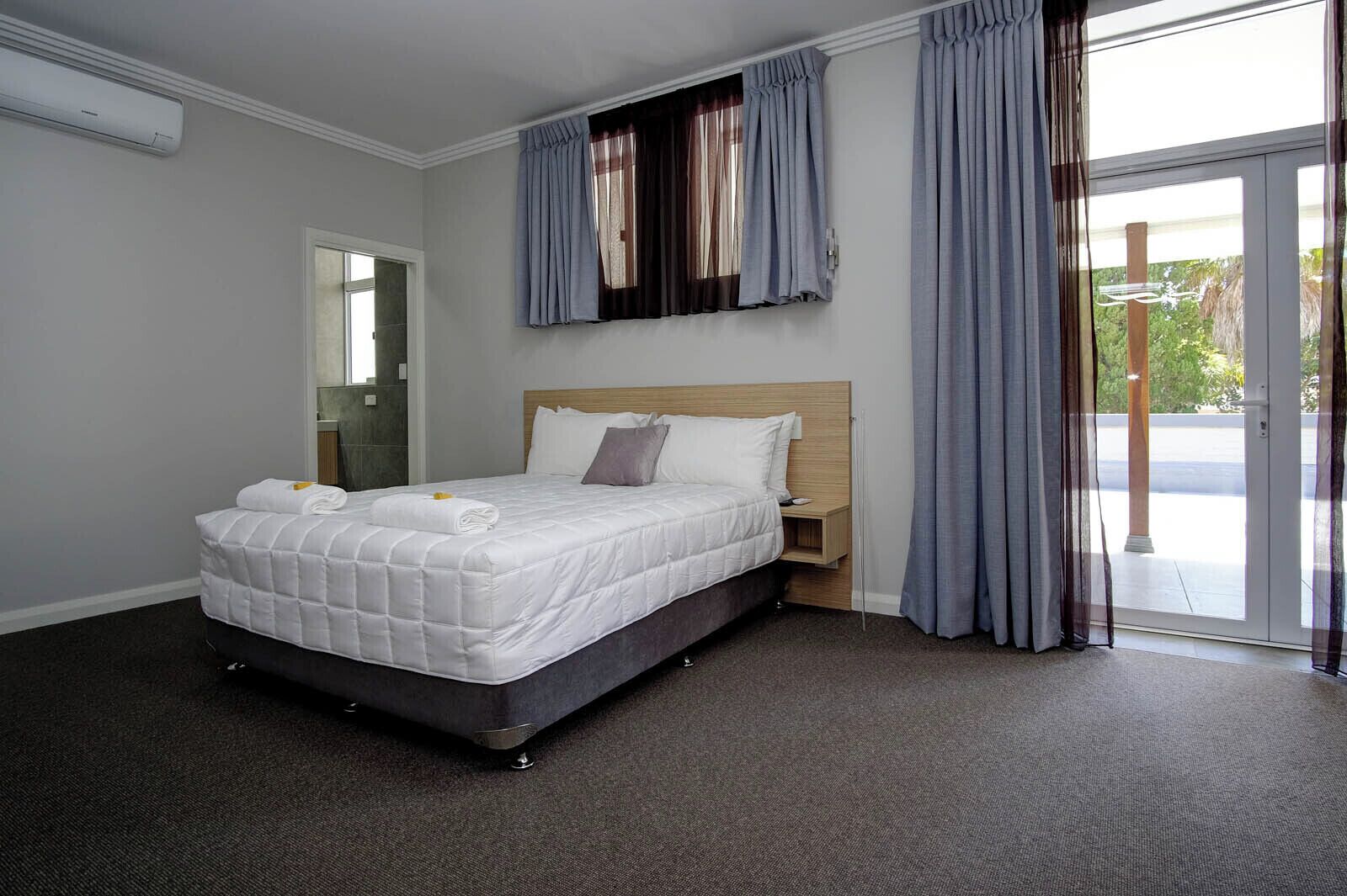 Ein Hotelzimmer mit einem Bett, einem Nachttisch, einem Spiegel und einer Schiebeglastür nach draußen.