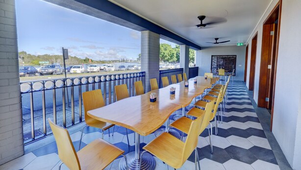 A long table with chairs in a covered area with a view of a parking lot. - Lakes and Ocean Hotel Forster (Forster)