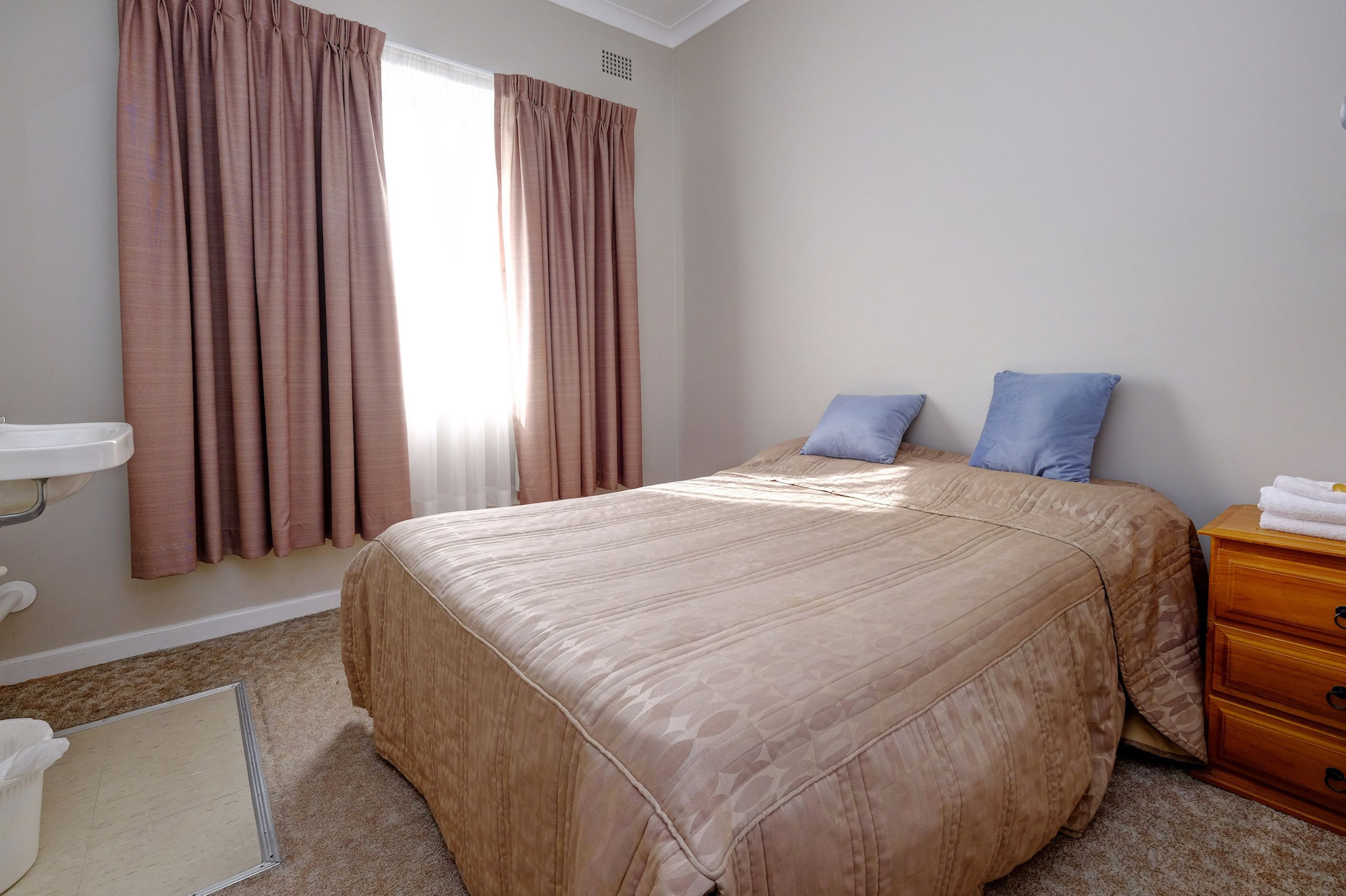 A bedroom with a large bed, a wooden dresser, a white sink, and a window with curtains.