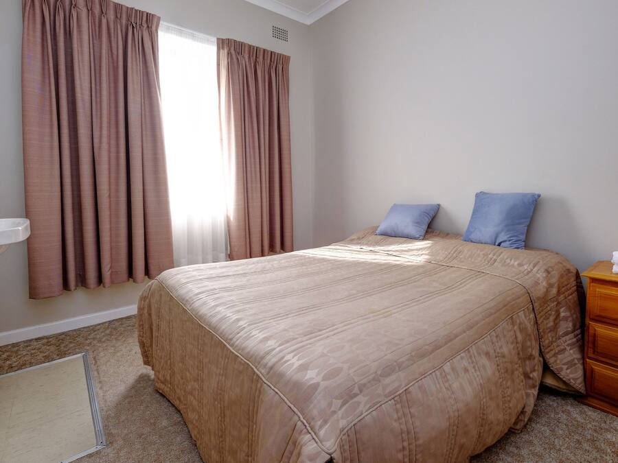 A bedroom with a large bed, a wooden dresser, a white sink, and a window with curtains.