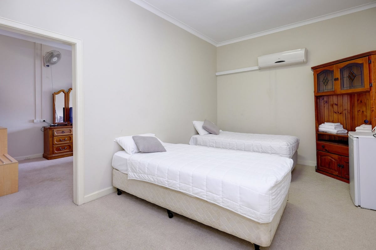 A bedroom with two single beds, a wooden wardrobe, a white air conditioner, and a mirror.