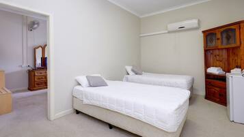Quarto com duas camas de solteiro, um guarda-roupa de madeira, um ar condicionado branco e um espelho.