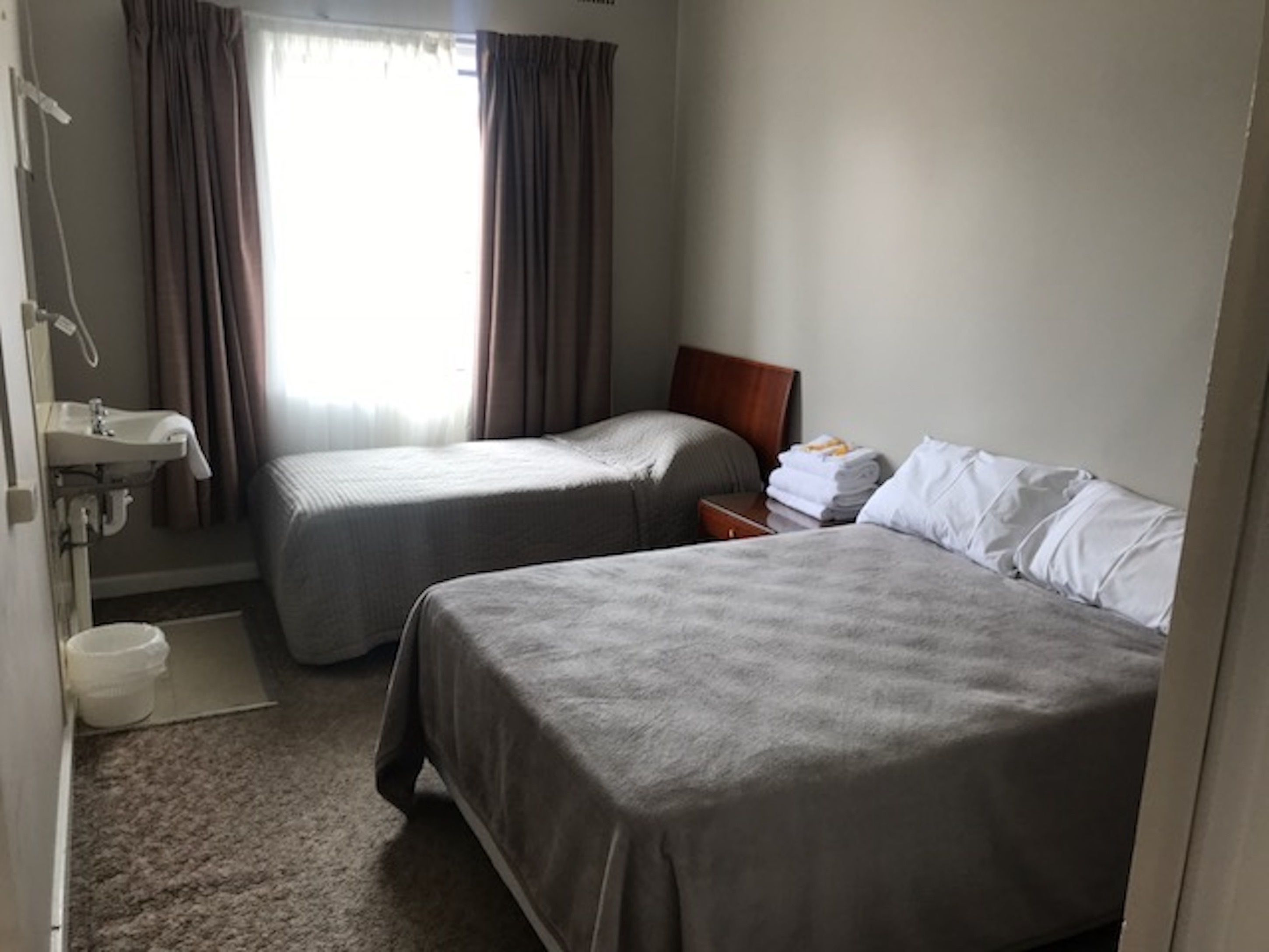 A hotel room with two beds, a bathroom with a sink, and a window with curtains.