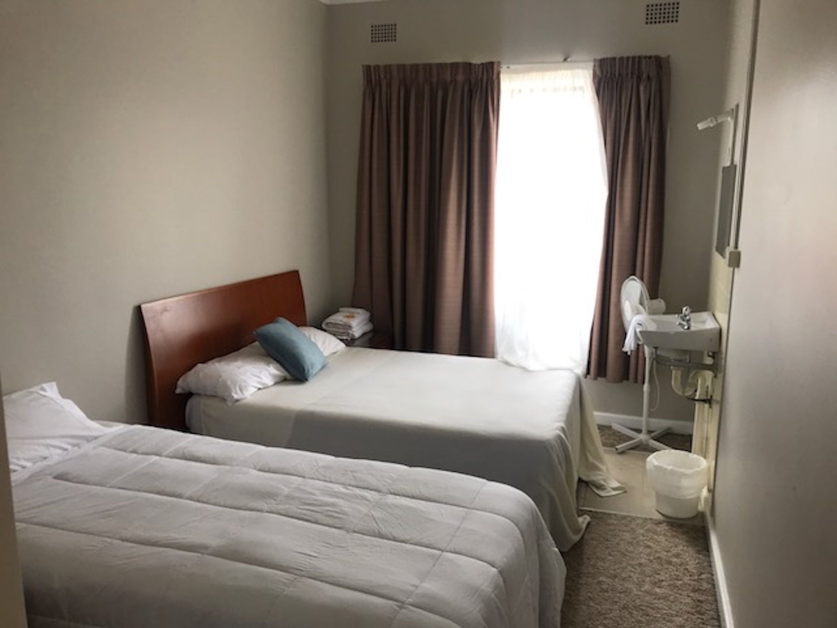 Habitación de hotel con dos camas, una mesita de noche con lámpara, una ventana con cortinas y un baño con lavabo y espejo.