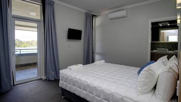 Hotelkamer met een bed, een flatscreen-tv, een raam met gordijnen, een airconditioning en een badkamer met een wastafel en spiegel.