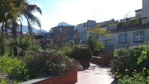 Un sendero bordeado de vegetación y paredes de ladrillo, que conduce a edificios residenciales con ventanas y balcones visibles.