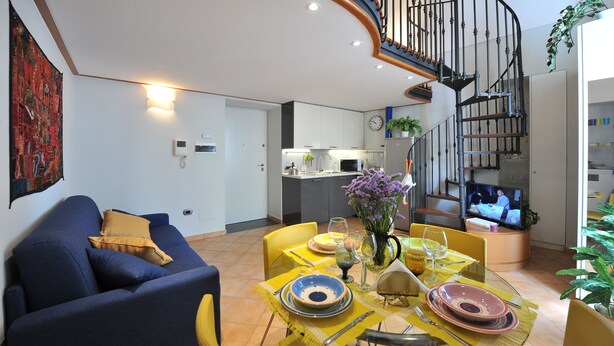 Una sala moderna con un sofá azul, un juego de comedor amarillo y una escalera en espiral.