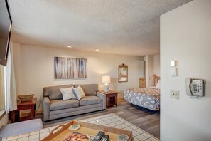A compact hotel room with a sofa, a bed, a bedside table with a lamp, a telephone, and a wall-mounted TV. - Liftside Studio (Breckenridge)