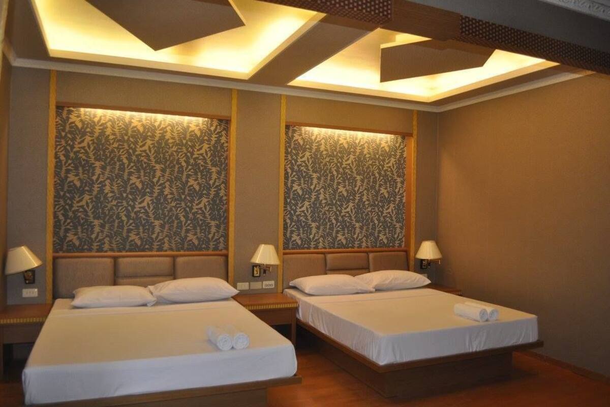 A hotel room with two beds, each with a headboard, bedside lamps, and a patterned wallpaper.