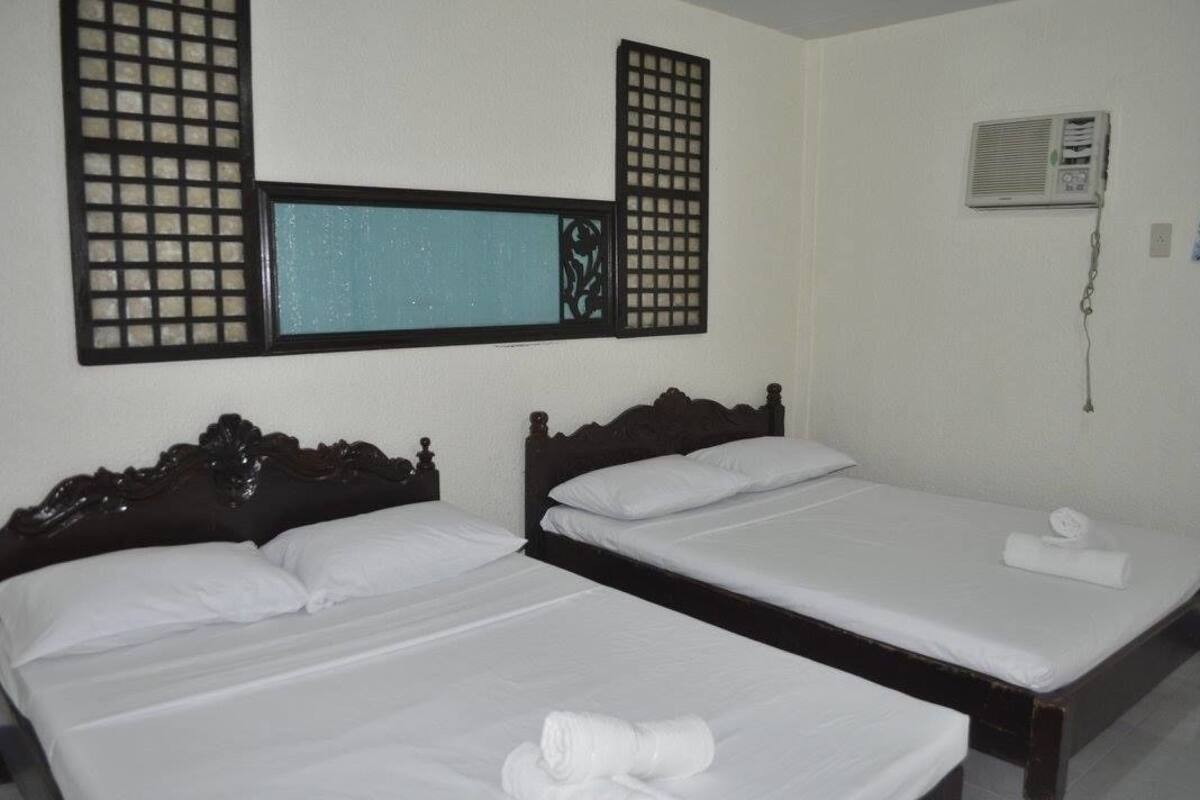 A hotel room with two beds, a window with a decorative screen, and an air conditioning unit on the wall.