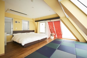 Un dormitorio con una cama grande, piso de madera, una ventana con cortina roja y un tragaluz.
