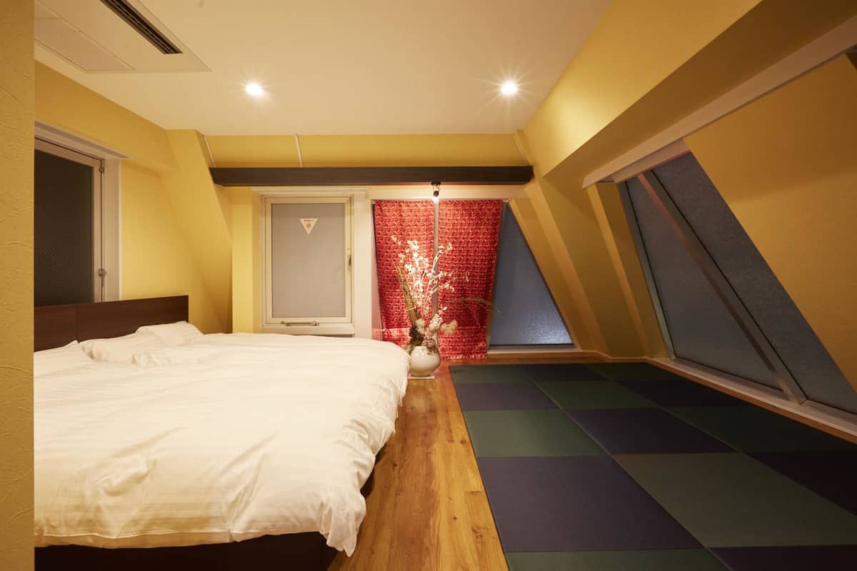 Quarto com cama, janela com cortina vermelha e vista para o exterior.