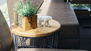 A cozy seating area with a cushioned bench, a small round table with a plant and a polar bear figurine, and a brick wall in the background. - Bed & Breakfast RENGA – Hostel (Tokyo)