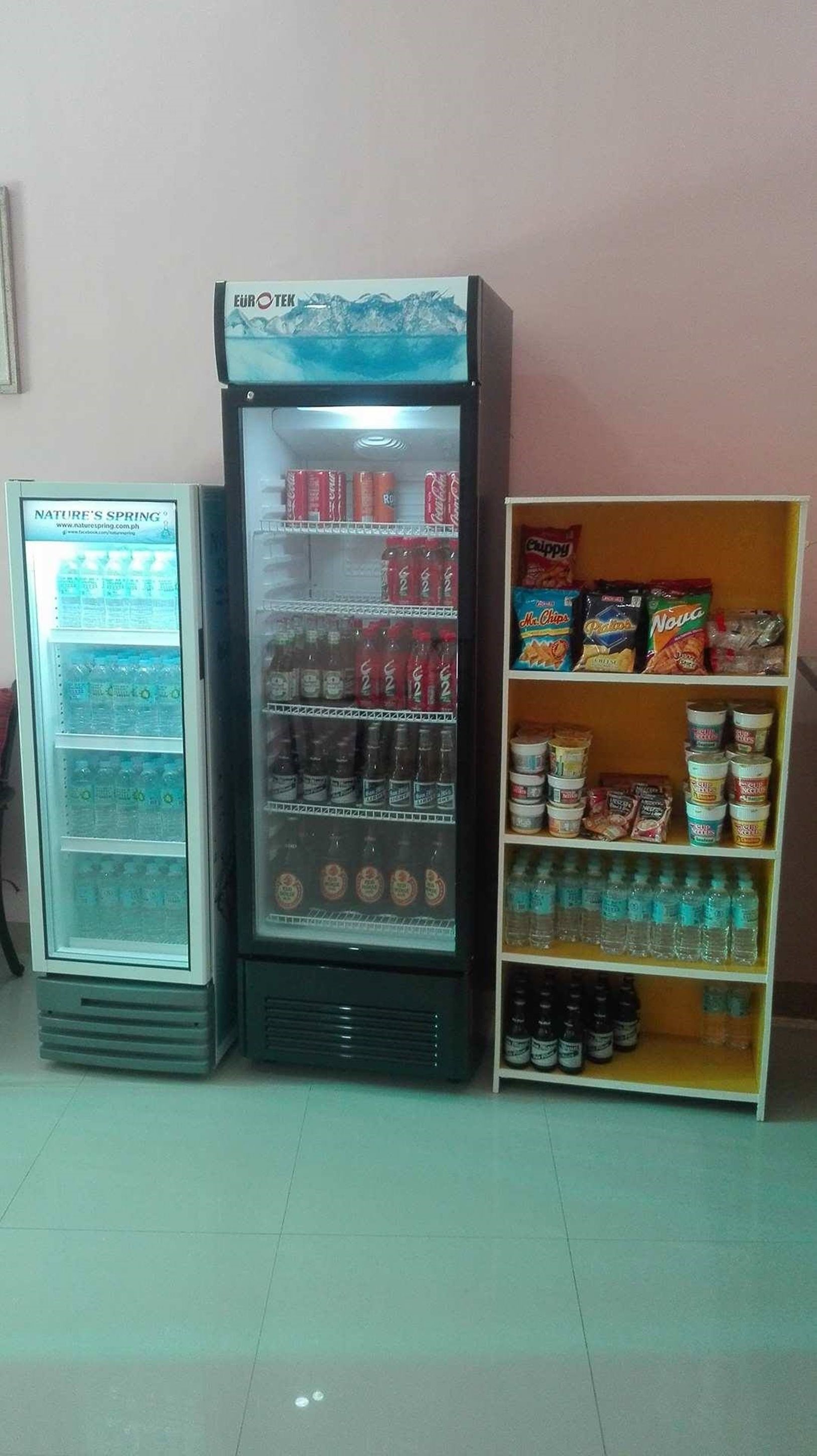 A vending machine with beverages and snacks, a refrigerator with drinks, and a shelf with packaged goods.
