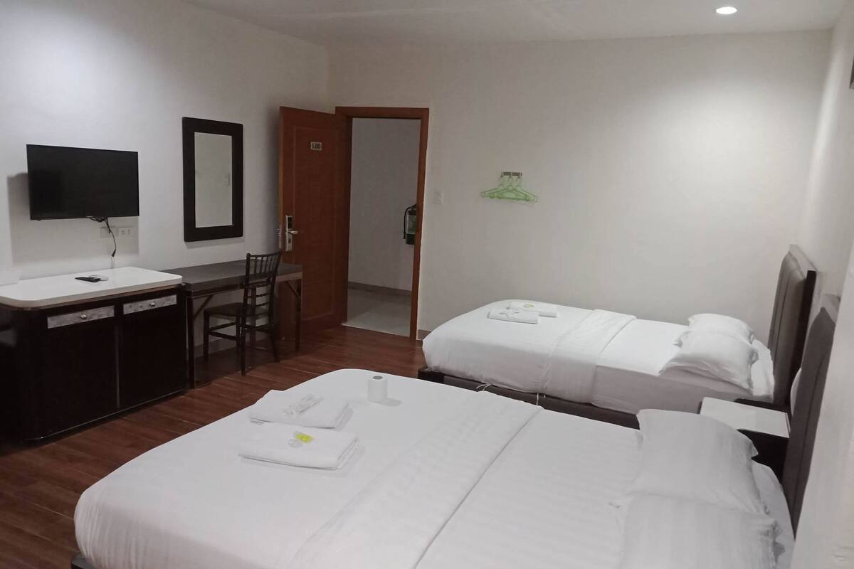 A hotel room with two beds, a desk, a chair, a TV, and a door.