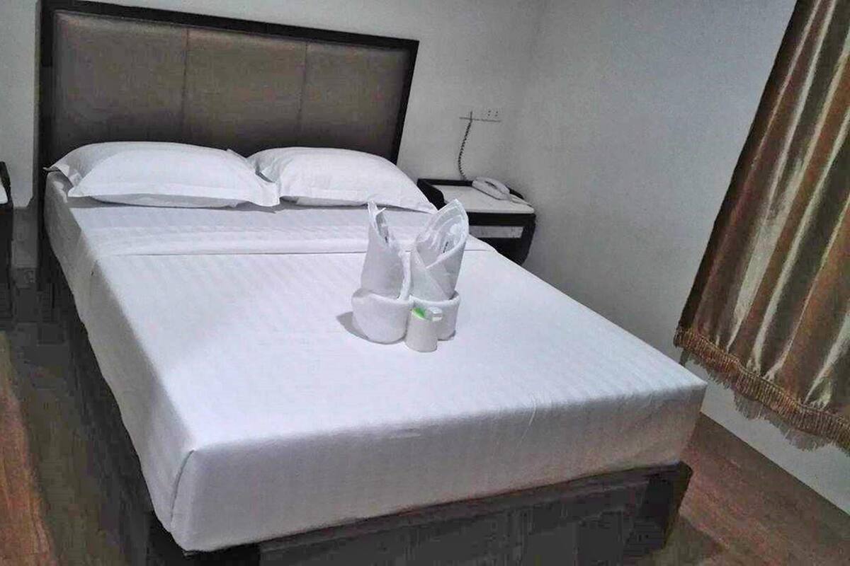 A hotel room with a neatly made bed, two bedside tables, and a telephone on one of the tables.