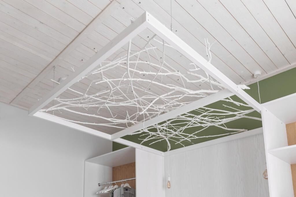 A room with a white ceiling and a green wall, featuring a white, branch-like structure hanging from the ceiling.