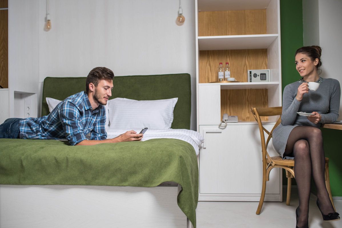 Un dormitorio con una cama verde, una mesita de noche blanca y una silla.