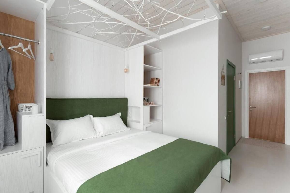 Une chambre à coucher avec un lit, des murs blancs, une tête de lit verte, une armoire blanche et une couvre-lit verte.