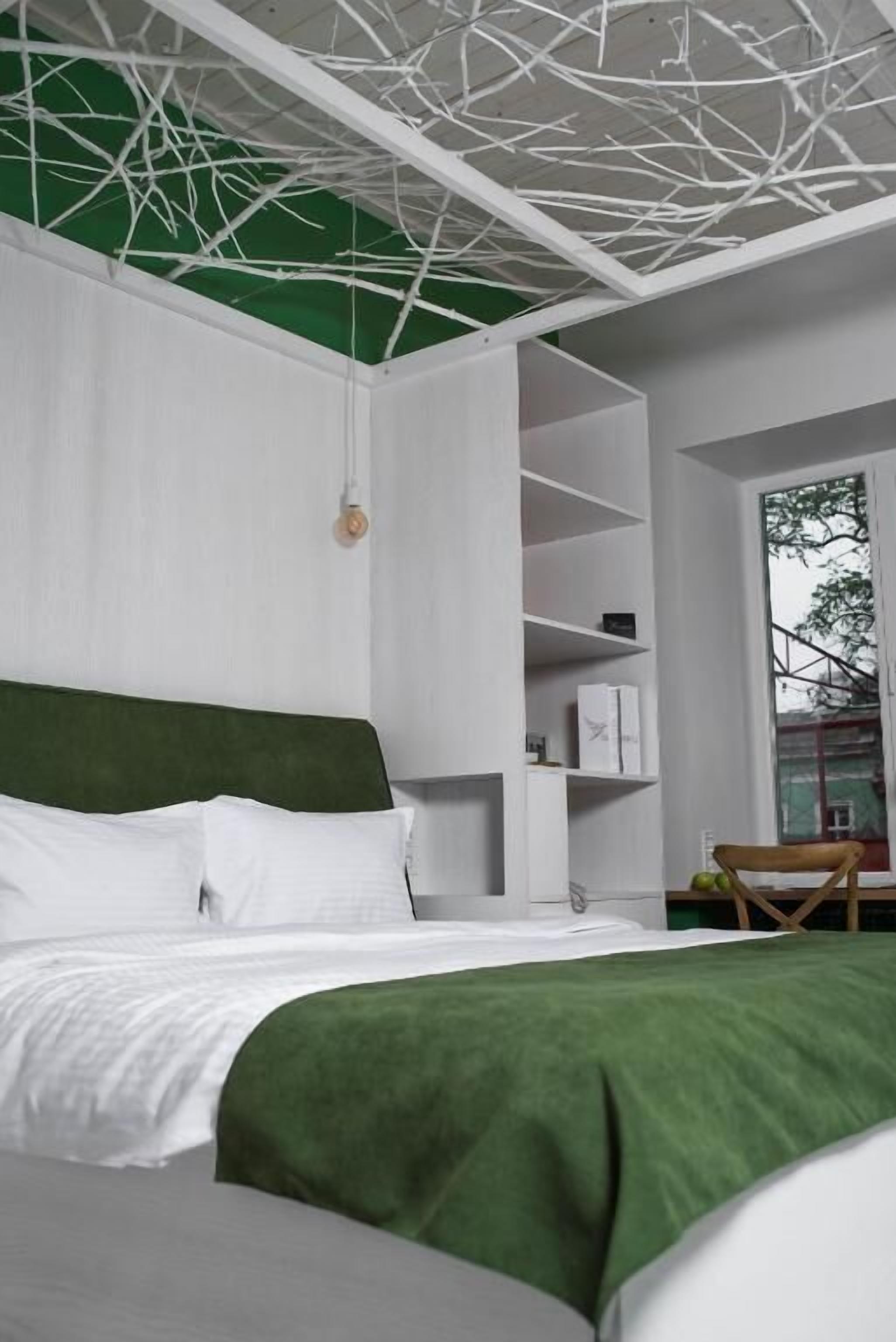 A modern bedroom with a green headboard, white bedding, and a white shelving unit against the wall.