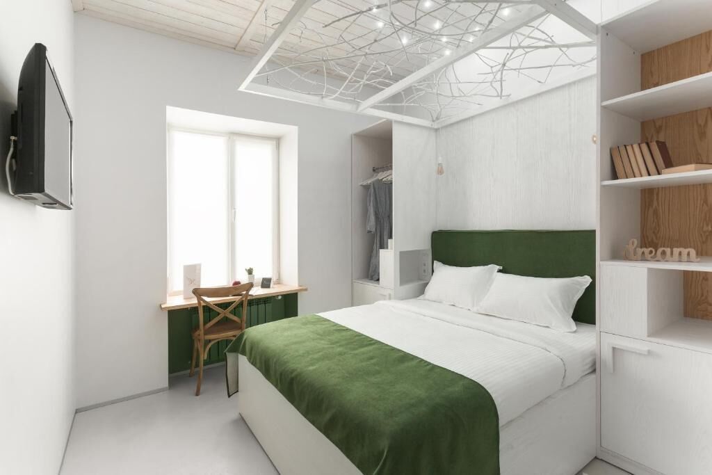A modern bedroom with a green bedspread, a desk with a chair, a wardrobe, and a TV mounted on the wall.