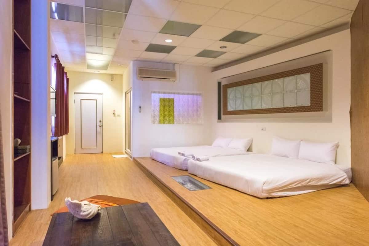 A hotel room with two beds, a wooden floor, a small table, and a window with a view.