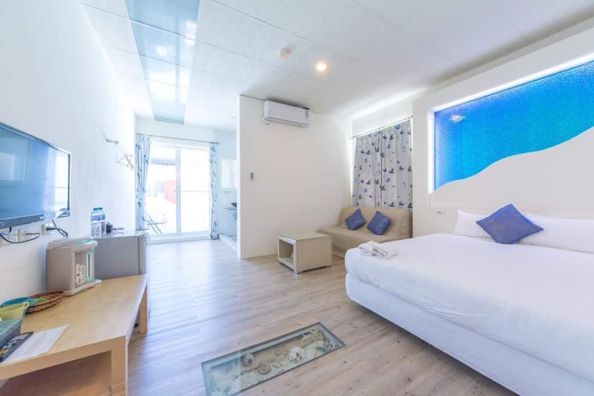A hotel room with a bed, a desk, a television, and a large window with curtains.
