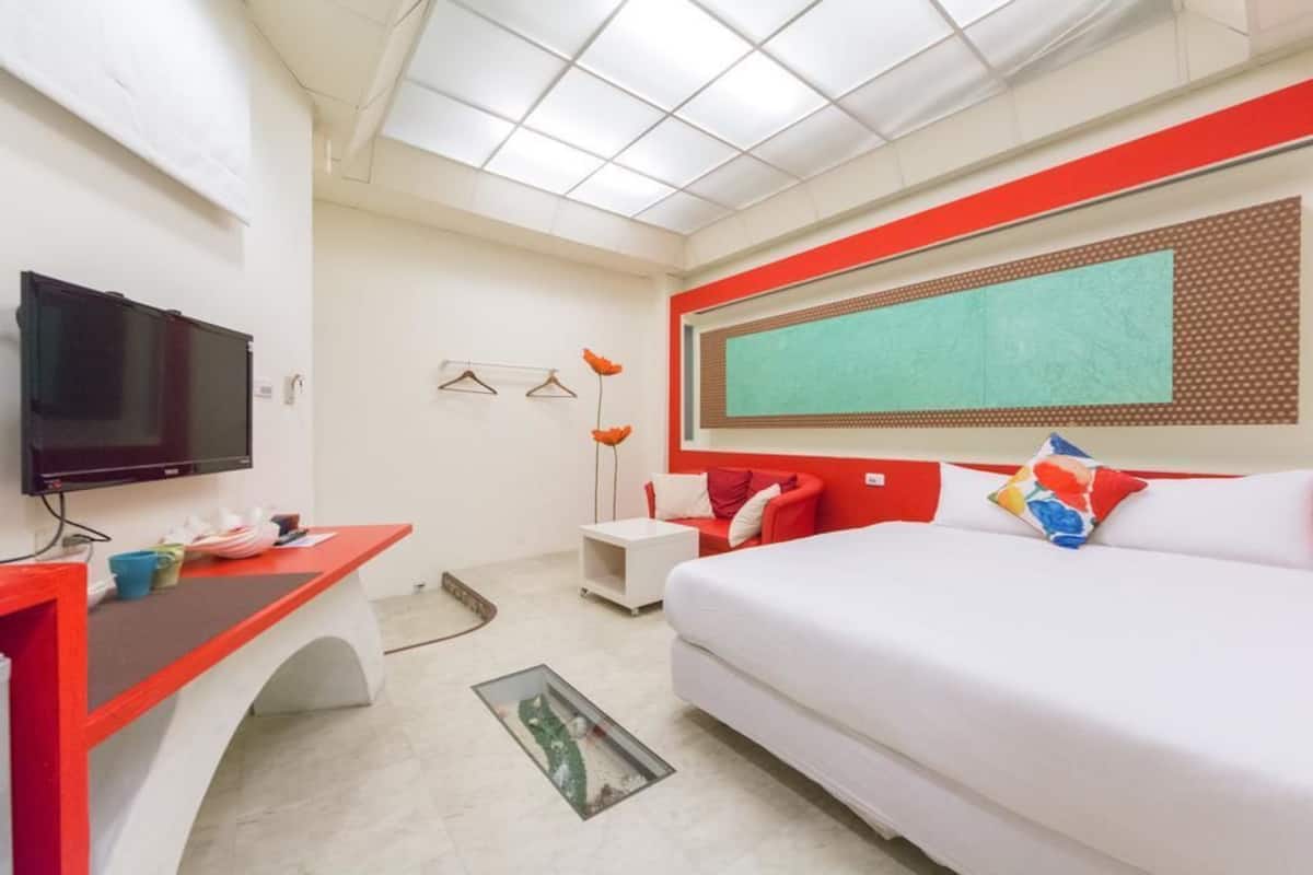 A modern hotel room with a large bed, a desk with a flat-screen TV, a small side table, and a window with a view.
