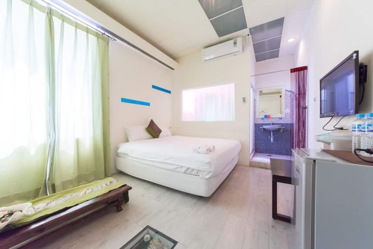 A hotel room with a bed, a desk, a television, and a bathroom visible through an open door.