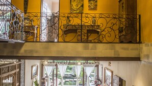 A spacious, well-lit interior with a high ceiling, a balcony with wrought iron railings, and a seating area with a sofa and cushions. - Avalon Ubud Villas (Ubud)