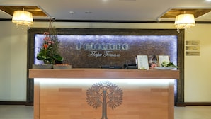 A reception desk with a wooden finish, a decorative tree emblem, and a backdrop with a textured wall and a sign indicating a restaurant and spa reception.
