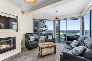 A modern living room with a fireplace, comfortable seating, and large windows offering a view of the outdoors. - Bonnies of Beachport (Beachport)