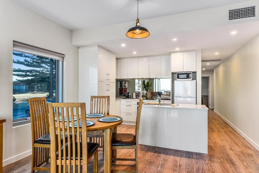 Une cuisine moderne avec des meubles blancs, un îlot central et un coin repas doté de chaises en bois.