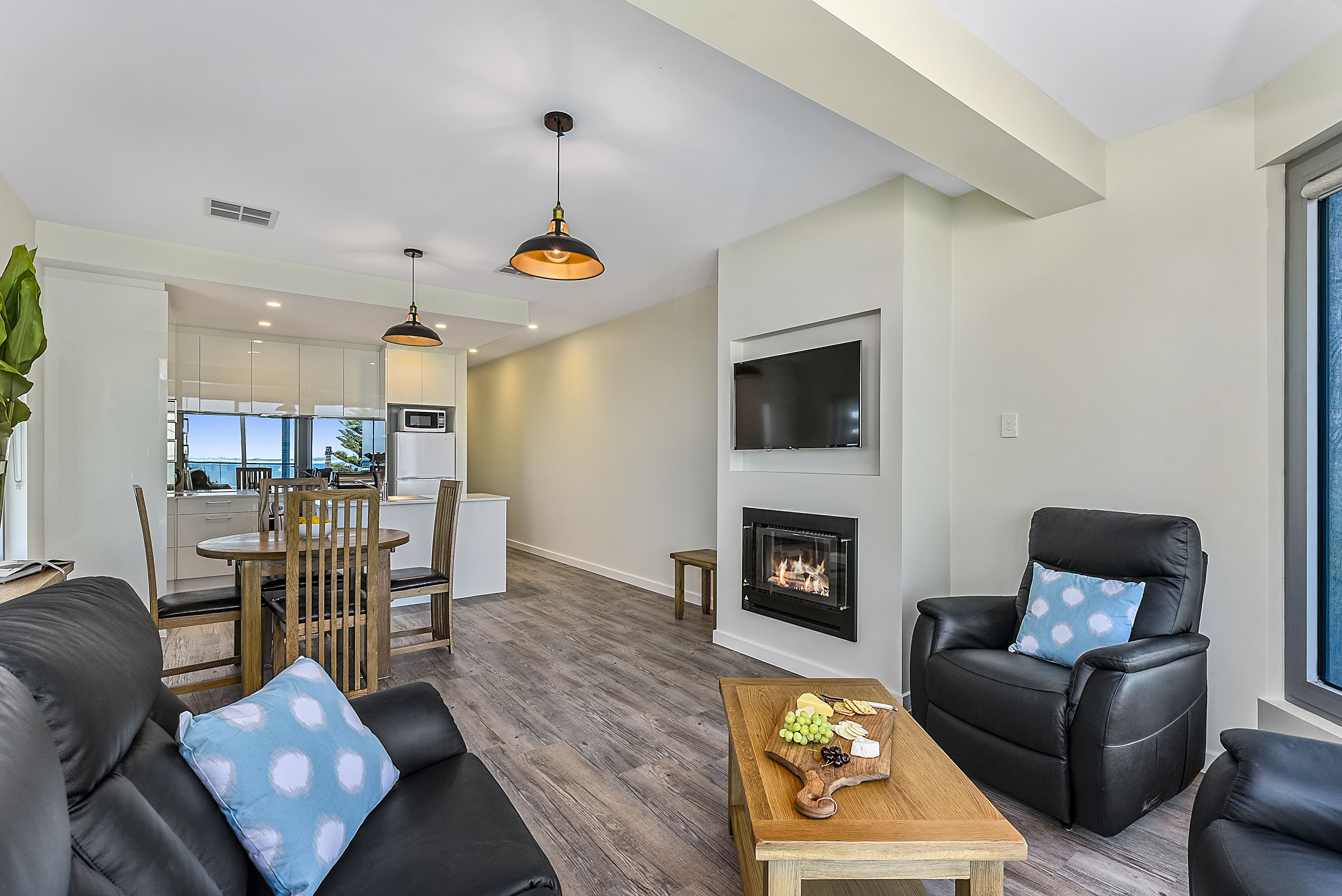 Una sala de estar moderna con chimenea, sofá de cuero negro, comedor y televisor montado en la pared.