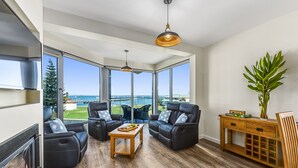 Uma sala de estar moderna com lareira, sofás de couro, uma mesa de centro de madeira e janelas amplas com vista para o exterior.