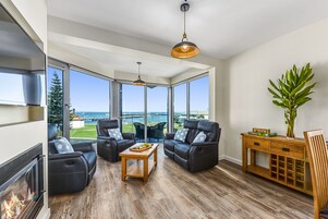 Una sala de estar moderna con chimenea, sofás de cuero, una mesa de centro de madera y grandes ventanales con vistas al exterior.