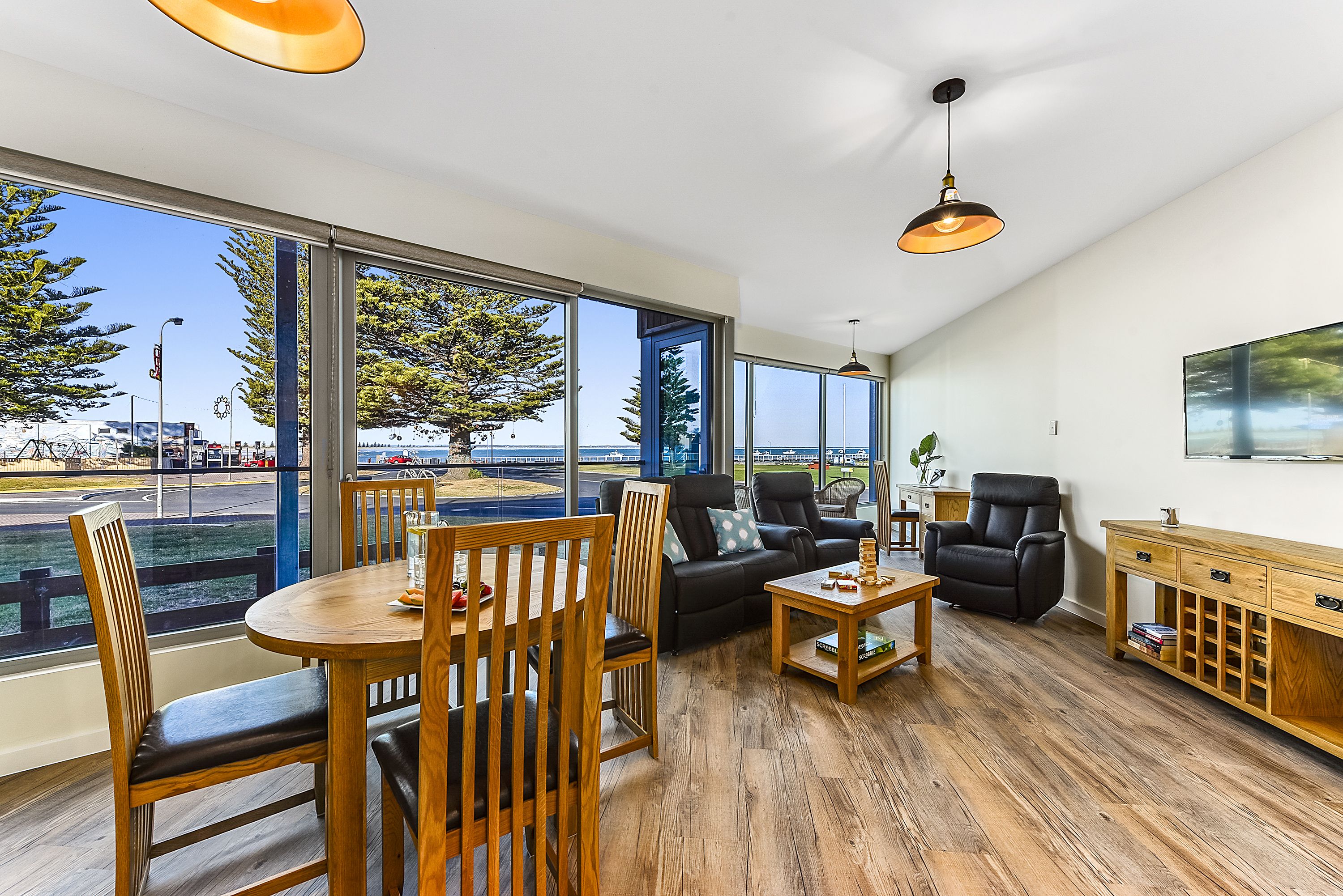 Amplio salón con ventana grande, muebles de madera y vistas a un parque y una calle.