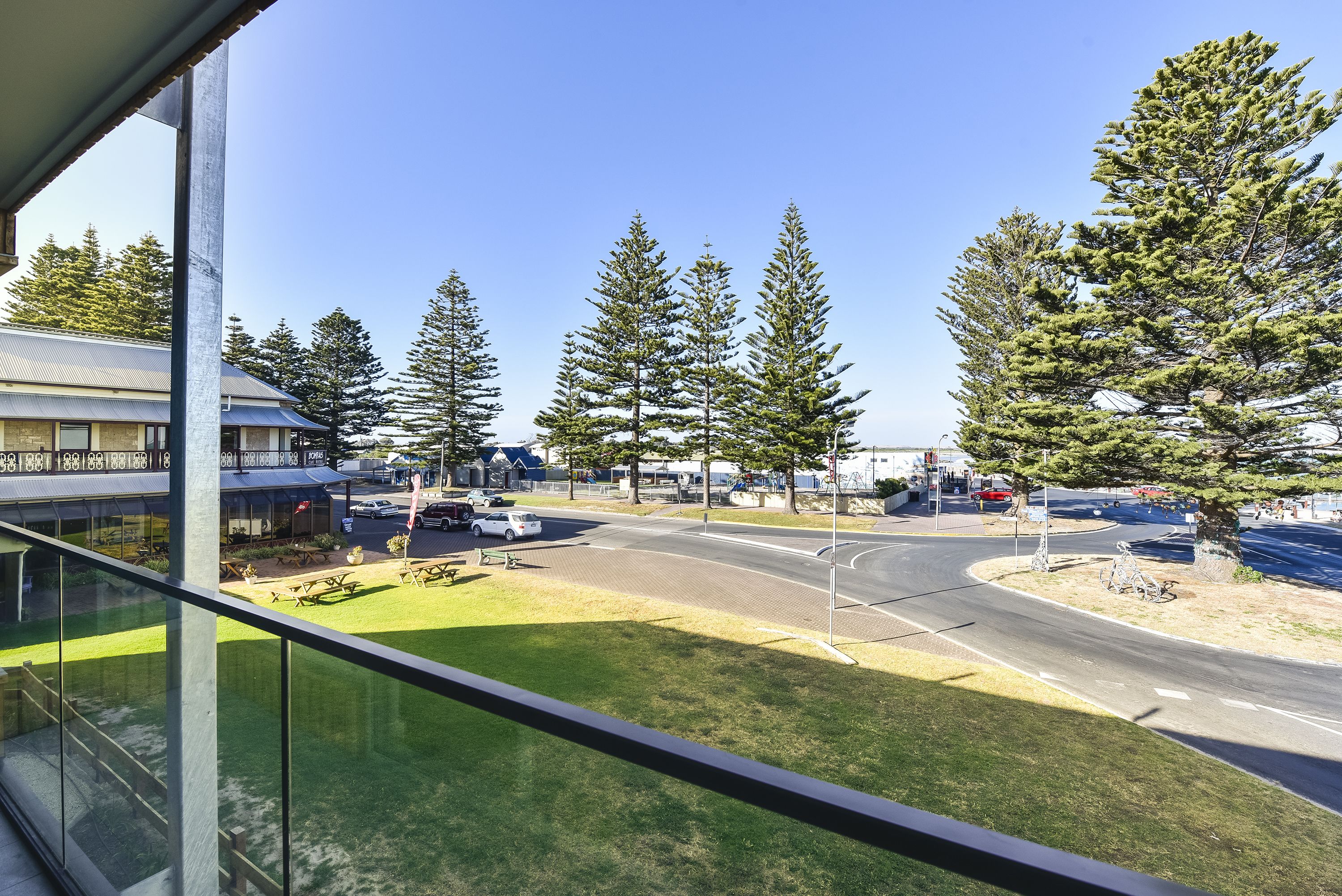 A view from a window overlooking a road with trees, a grassy area, and a building with a blue roof.