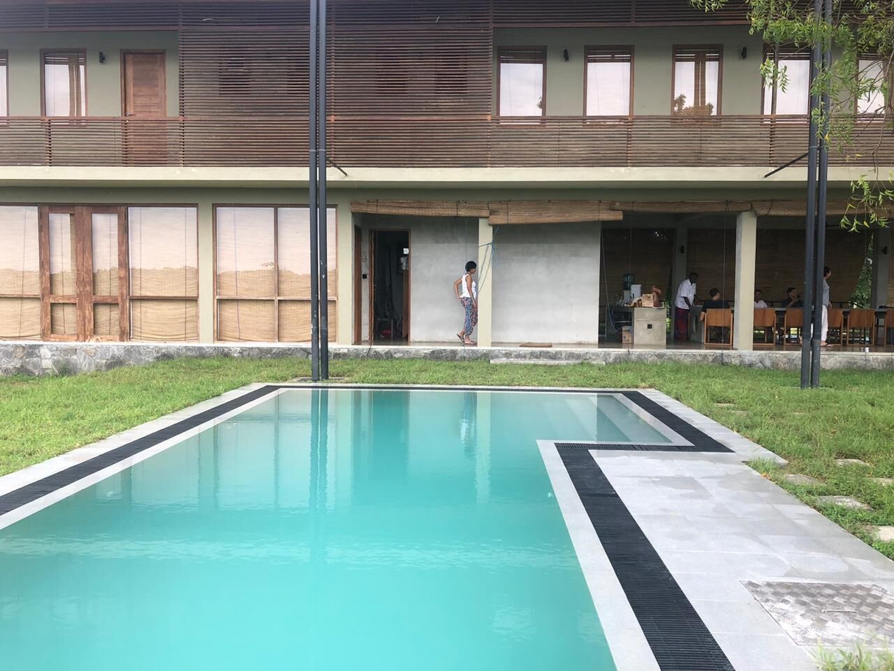 A swimming pool with a tiled deck, a building with a flat roof and large windows, and a grassy area.