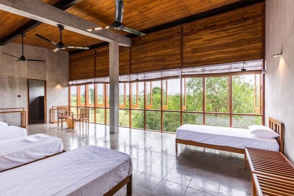 A spacious room with two beds, a wooden ceiling, large windows, and a view of greenery. - Tree Tops Yala (Kirinda)