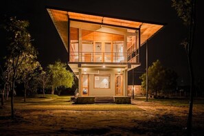 A two-story building with a balcony, a staircase, and a well-lit entrance. - Tree Tops Yala (Kirinda)
