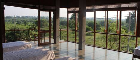 A spacious room with large windows offering a view of a lush landscape. There are two beds with white linens.