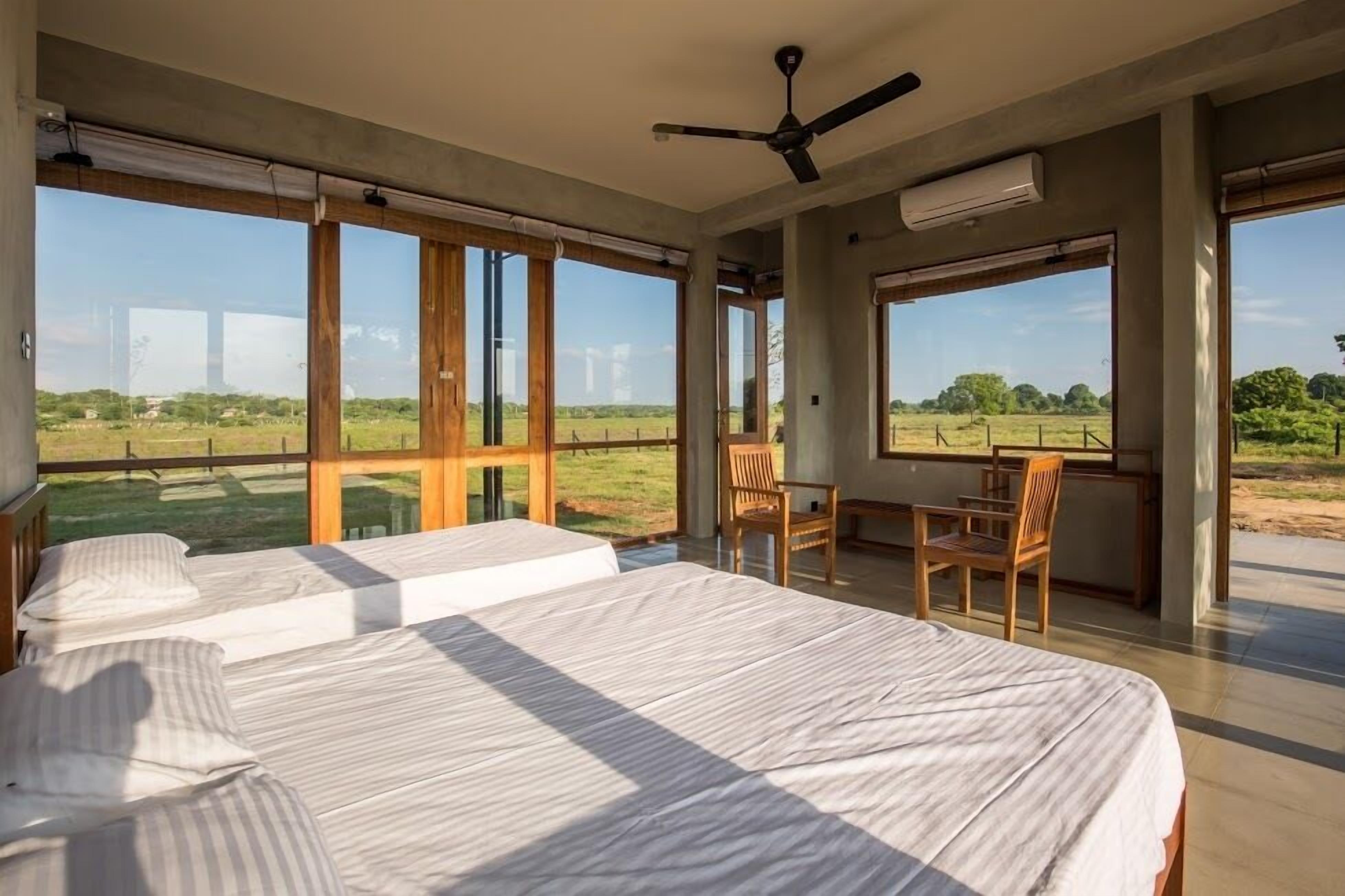 Ein Schlafzimmer mit zwei Betten, einem Schreibtisch und einem Stuhl, große Fenster mit Blick ins Grüne.