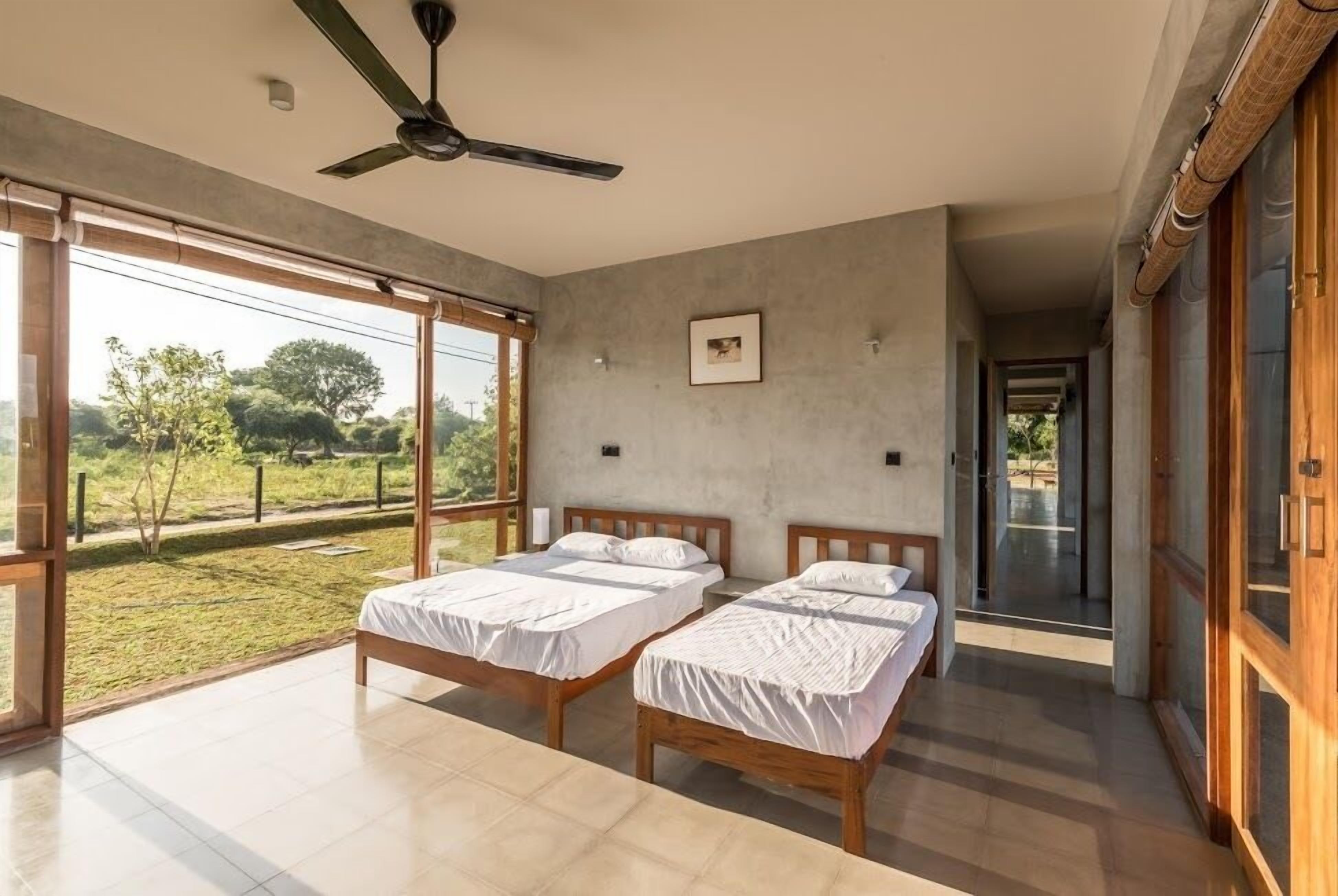 Un dormitorio moderno con dos camas, ventanas amplias y un ventilador de techo.
