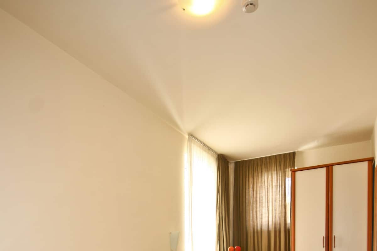 A bedroom with a wooden bed, a wardrobe, and a window with curtains.